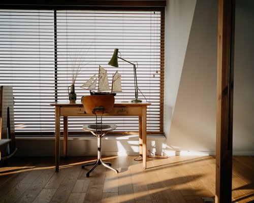 A notebook and reading glasses resting on a wooden desk near a window